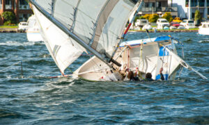 A girl and boy in the water climbing back into a capsized sinking sailboat.