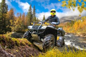 Driver on helmet riding ATV near waterfall.